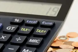 Kalkulator z klawiszami "TAX+", "TAX-" i "Euro" obok stosu monet. Czas na rozliczenie działalności gospodarczej do kiedy?