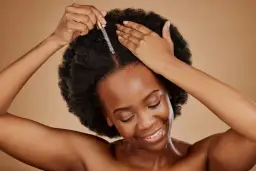Kobieta z afro włosami aplikuje olejek na skórę głowy. Idealne olejowanie włosów średnioporowatych dla zdrowego blasku.