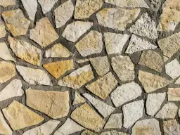 Kamienna ściana z nieregularnych, żółtawych i białych kamieni. Piaskowiec tworzy naturalną, rustykalną mozaikę.