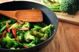 Brokuły, groszek cukrowy i papryczka chili w woku, gotowe do stir fry. Drewniana łopatka miesza warzywa.