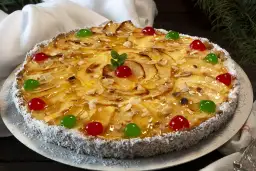Tarta de manzana con crema pastelera, decorada con almendras laminadas, cerezas rojas y verdes, y coco rallado en el borde.