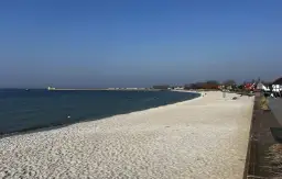 Piękna plaża, idealna na rejs z Gdańska na Hel. W oddali widać falochron i zabudowania.