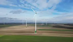Wiatraki na tle błękitnego nieba z chmurami, na tle pól uprawnych.