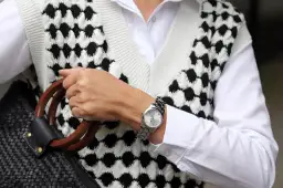 Elegancki zegarek na sztywnej bransolecie, dopełniający stylizację z białą koszulą i kamizelką w czarno-białe wzory.