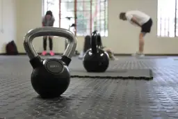Kettlebell 8kg na siłowni, w tle ćwiczący ludzie.