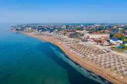 Plaża nad Morzem Czarnym z rzędami leżaków i parasoli. W tle zabudowania kurortu. Woda wygląda na ciepłą, idealną do kąpieli.