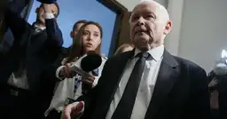 Starszy mężczyzna w garniturze, otoczony przez dziennikarzy z mikrofonem TVP Info, być może odpowiada na pytanie: co złego zrobił PiS?
