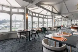 Salle de restaurant lumineuse avec vue sur le port, tables dressées et chaises modernes.