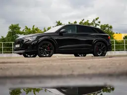 Czarny Audi Q9 z czerwonymi zaciskami hamulcowymi, odbijający się w kałuży. Sprawdź audi q9 cena!