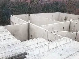 Budowa domu w toku. Widać betonowe ściany i przygotowany do wylania strop filigran z siatką zbrojeniową.