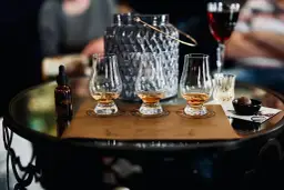 Degustacja whisky metodą tulipana: jak poczuć torf, wanilię i dym. Na stole kieliszki, buteleczka z whisky i czekoladka.