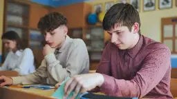 Uczniowie siedzą przy ławkach w klasie, jeden z nich przegląda notatki.