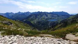 Widok na Tatry z kamienistego zbocza. W dole jeziora i kręte szlaki na krzyżne, otoczone zielenią i skalistymi szczytami.
