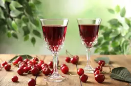 Dwa kieliszki z rubinowym alkoholem z wiśni, otoczone świeżymi owocami i zielonymi liśćmi.