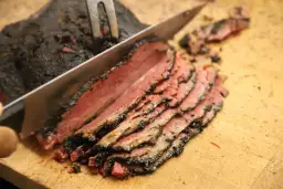 Un cuchillo corta un trozo de pastrami ahumado y jugoso, revelando su interior rosado.