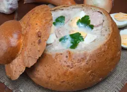 Pyszny żurek w chlebie, z kiełbasą i jajkiem, ozdobiony natką pietruszki. Idealny na polski obiad.
