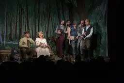 Aktorzy na scenie, w tle las. Rozmowy przy wycinaniu lasu, gdy grupa ludzi w strojach z epoki dyskutuje.