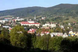 Widok na Ustrzyki Dolne z górami w tle. Miasto z czerwonymi dachami i nowoczesnymi budynkami, otoczone zielenią. Atrakcje turystyczne czekają!