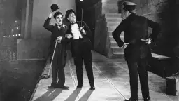 Charlie Chaplin i jego towarzysz w eleganckich strojach, z kapeluszami i laskami, w scenie z okresu kina niemego. Policjant stoi tyłem.