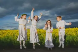Cztery dzieci w strojach komunijnych skaczą na tle kwitnącego pola rzepaku.