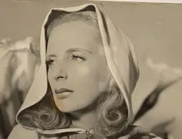 Portret Tamary Łempickiej w nakryciu głowy, z lokami opadającymi na ramiona.