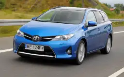 Niebieski Toyota Auris 1.6 benzyna w wersji kombi jedzie po drodze.