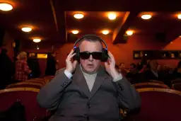 Mężczyzna w okularach i słuchawkach, słucha audiodeskrypcji w kinie.