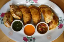 Empanadas de carne doradas y crujientes, servidas con tres salsas: chimichurri, picante y criolla.