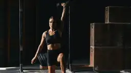 Kobieta w stroju sportowym podnosi hantle nad głowę w siłowni.