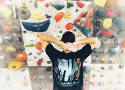 Wspinaczka bouldering na kolorowej ściance. Mężczyzna z rękami za głową, przygotowuje się do pokonania trudnej trasy.