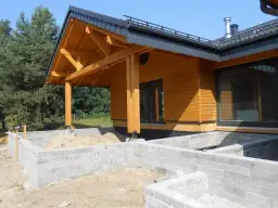 Drewniany dach płatwiowo krokwiowy nad wejściem do domu w budowie. Fundamenty z bloczków betonowych.