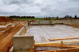 Fundament domu w budowie, z betonowymi ścianami, siatką zbrojeniową i folią na ziemi.