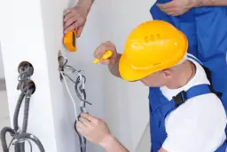 Elektryk w żółtym kasku pracuje przy instalacji, zastanawiając się, ile zarabia elektryk w Norwegii.