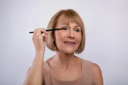 Mujer mayor aplicando sombra de ojos con brocha, aprendiendo como maquillar los ojos a partir de los 50 años para realzar su belleza natural.