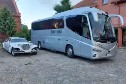 Biała limuzyna i szary autokar stoją obok siebie na brukowanym dziedzińcu.