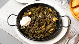 Arroz negro con sepia, un plato de mariscos oscuro y sabroso, servido en una paellera con una cucharada de alioli.