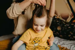 Mama delikatnie rozczesuje kołtuny u dziecka, które uśmiecha się, patrząc w dół.