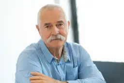 Portret starszego mężczyzny z siwymi włosami i wąsami, w niebieskiej koszuli.