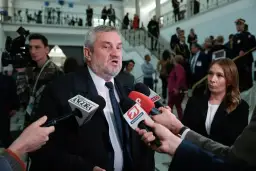 Mężczyzna z siwą brodą, przypominający ojca Agnieszki Pomaskiej, udziela wywiadu dziennikarzom.