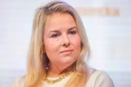 Kamila Kalinczak z blond włosami i złotym naszyjnikiem, patrzy w bok.
