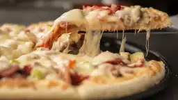 Gorąca, ciągnąca się pizza mrożona z serem, szynką i ananasem. Kawałek pizzy jest podnoszony, odsłaniając roztopiony ser.