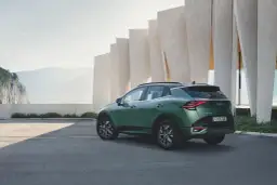 Zielony samochód Kia Sportage zaparkowany przed nowoczesnym budynkiem z elementami skalnymi w tle.