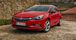 Czerwony Opel Astra Sports Tourer zaparkowany na kamienistej nawierzchni, z kamiennym murem w tle.