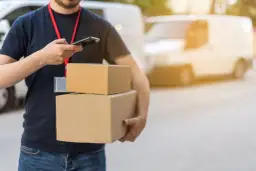 Livreur avec colis, vérifiant son téléphone. Un retard de livraison peut être une violation du code de la consommation.