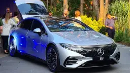 Srebrny Mercedes EQS z niebieskim podświetleniem prezentuje się efektownie na tle zieleni.