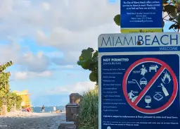 Miami Floryda Stany Zjednoczone: tablica z zakazami na plaży, w tle ocean i ratownicza wieża.