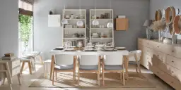 Jadalnia w stylu skandynawskim z białym stołem, szarymi krzesłami i regałami. Ściany w odcieniu pastelowy szary.