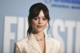 Jenna Ortega, uśmiechnięta, w białej koronkowej marynarce i efektownej biżuterii. Czy Jenna Ortega żyje? Tak, wygląda świetnie!