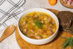 Aromaticzny kapuśniak ze słodkiej kapusty z kawałkami mięsa, ziemniakami i marchewką, udekorowany koperkiem. Obok kromki ciemnego chleba.