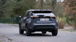 Szary Toyota Yaris Cross hybrydowy z tyłu na drodze.